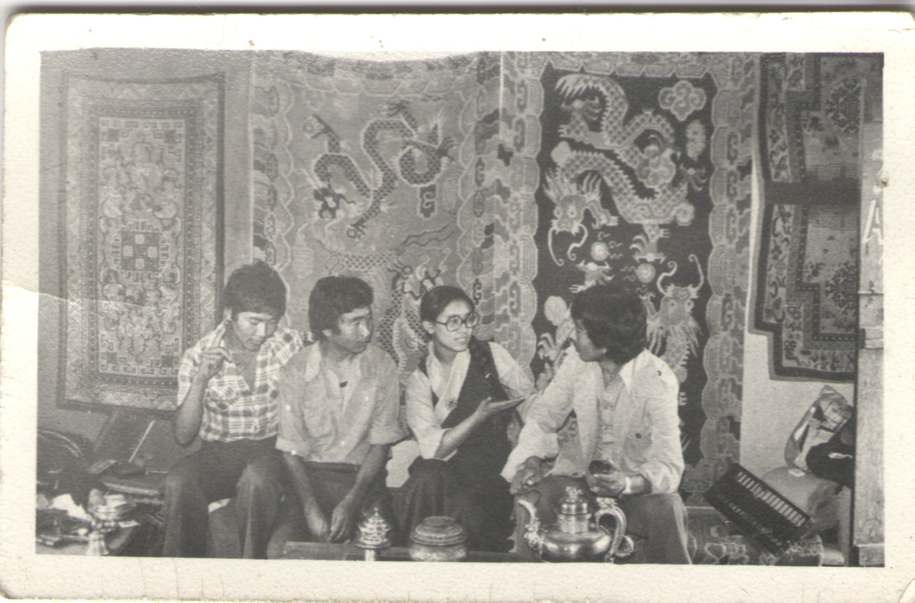 Vintage black and white photo of four people sitting together in a room with decorative wall hangings.
